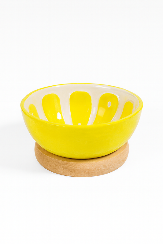 Żółta ceramiczna miseczka o błyszczącej powierzchni z białymi promienistymi wzorami wewnątrz, ustawiona na okrągłej drewnianej podstawce na białym tle – elegancka dekoracja stołu i praktyczne naczynie do serwowania