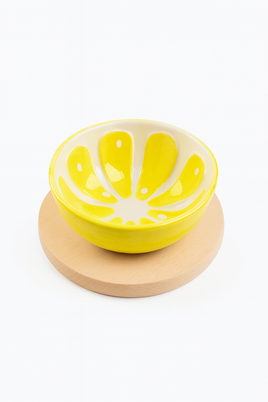 Żółta ceramiczna miseczka z białym wnętrzem w kształcie płatków, ustawiona na okrągłej desce z jasnego drewna bukowego – eleganczne i radosne połączenie kolorów idealne do kuchni.