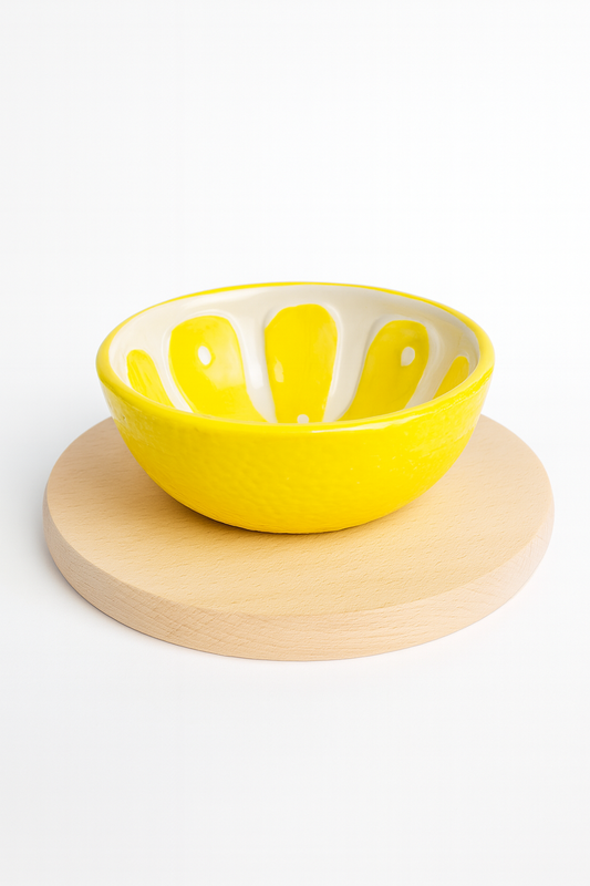 Ceramiczna miseczka w kształcie cytryny w intensywnym żółtym kolorze, ustawiona na okrągłej drewnianej desce bukowej — idealna do serwowania przekąsek lub ozdoby kuchni.
