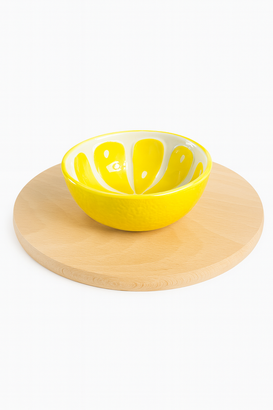Żółta ceramiczna miseczka w kształcie plastra cytryny ustawiona na okrągłej drewnianej desce – świeży akcent do serwowania przekąsek lub deserów.