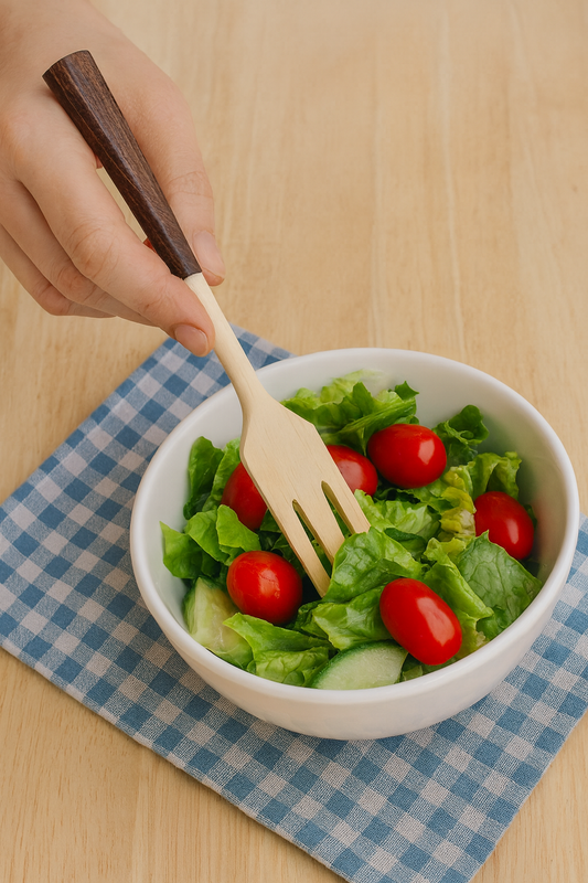 Drewniany widelec kuchenny z ciemną rączką miesza świeżą sałatkę z pomidorami i ogórkami w białej misce na drewnianym stole – naturalna, apetyczna aranżacja eco.