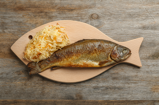 Drewniana deska do serwowania w kształcie ryby, na której podano upieczoną rybę z chrupiącą skórką oraz surówkę z kiszonej kapusty i marchewki, ustawioną na rustykalnym drewnianym stole – naturalny, apetyczny kadr produktowy w stylu e-commerce Chłopcy z Rancza.