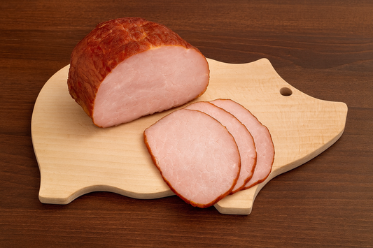 Drewniana deska kuchenna w kształcie świnki z soczystą upieczoną szynką i kilkoma plasterkami wędliny, ułożona na stole — produkt Chłopcy z Rancza.