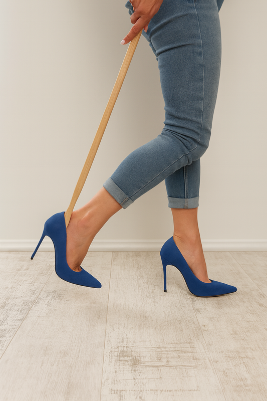 Kobieta zakłada eleganckie niebieskie szpilki przy pomocy dużej drewnianej łyżki do butów 63 cm – komfort, styl i praktyczność w jednym. Chłopcy z Rancza / Ranch Boys