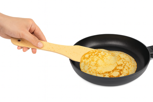 Kobieca ręka obraca złocistego naleśnika na patelni przy pomocy drewnianej łopatki o długości 29 cm i szerokości 5,5 cm, idealnej do przewracania naleśników i pancake’ów – Chłopcy z Rancza / Ranch Boys.