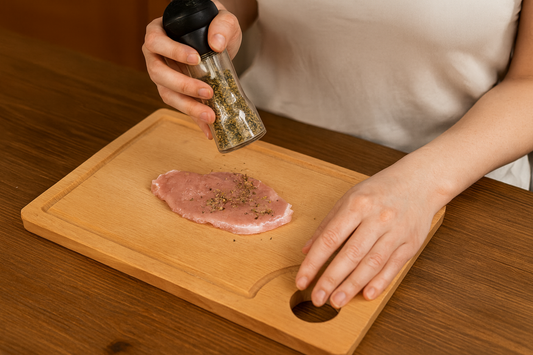 Kobieta przyprawia rozbitego kotleta schabowego na drewnianej desce z jasnego buku z rowkiem i otworem, leżącej na drewnianym stole – Chłopcy z Rancza