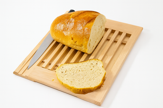 Drewniana deska do krojenia z rusztem na okruchy, wykonana z jasnego drewna bukowego. Na desce leży nóż do chleba oraz bochenek świeżego, chrupiącego chleba z odkrojonym plastrem.