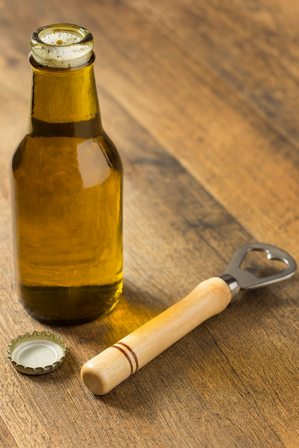 Drewniany otwieracz do butelek z metalową końcówką leży na drewnianym stole obok otwartej butelki piwa i zdjętego kapsla – naturalna, ciepła scena