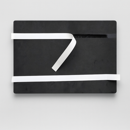 Czarna prostokątna tablica z delikatną fakturą, na której ułożone są dwie białe taśmy – jedna poziomo, druga ukośnie.